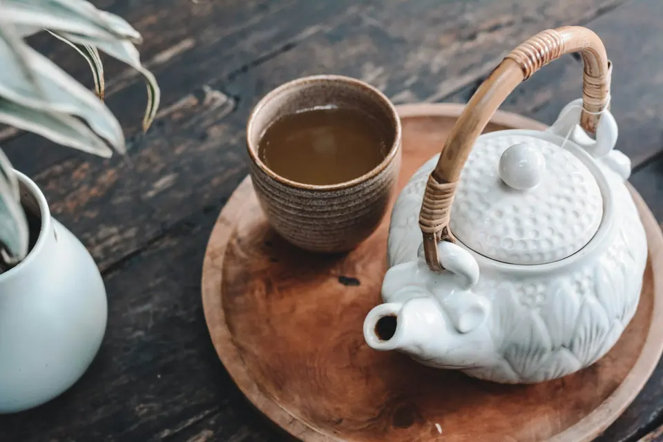 A textured ceramic teacup beside a white teapot with rattan handle.