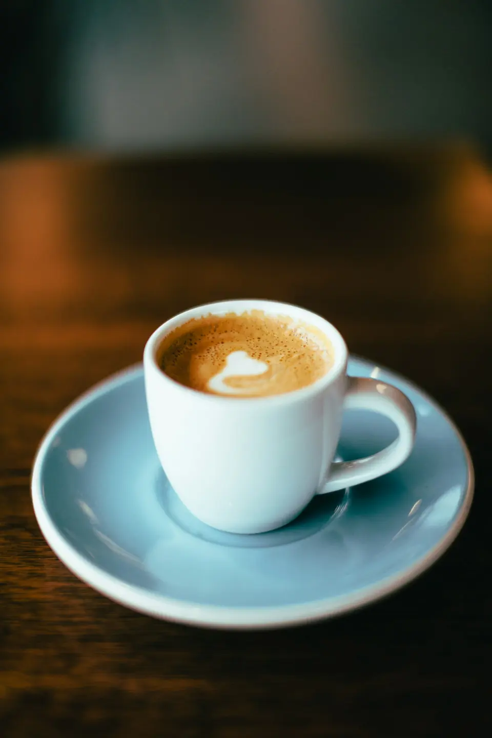 A single espresso shot in a white cup on a blue saucer.